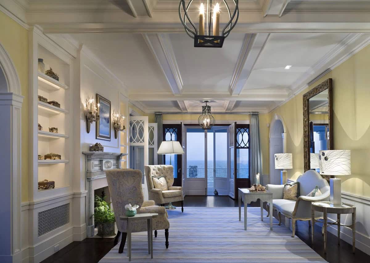 Elegant coastal living room with fireplace, built-in shelves, armchairs, and French doors opening to an ocean view