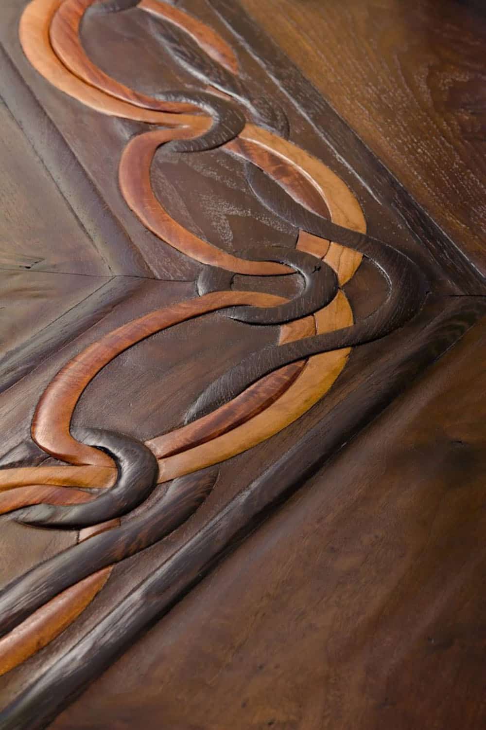 Close-up of hand-carved wood floor inlay with interlocking scrollwork design in contrasting dark and light wood tones