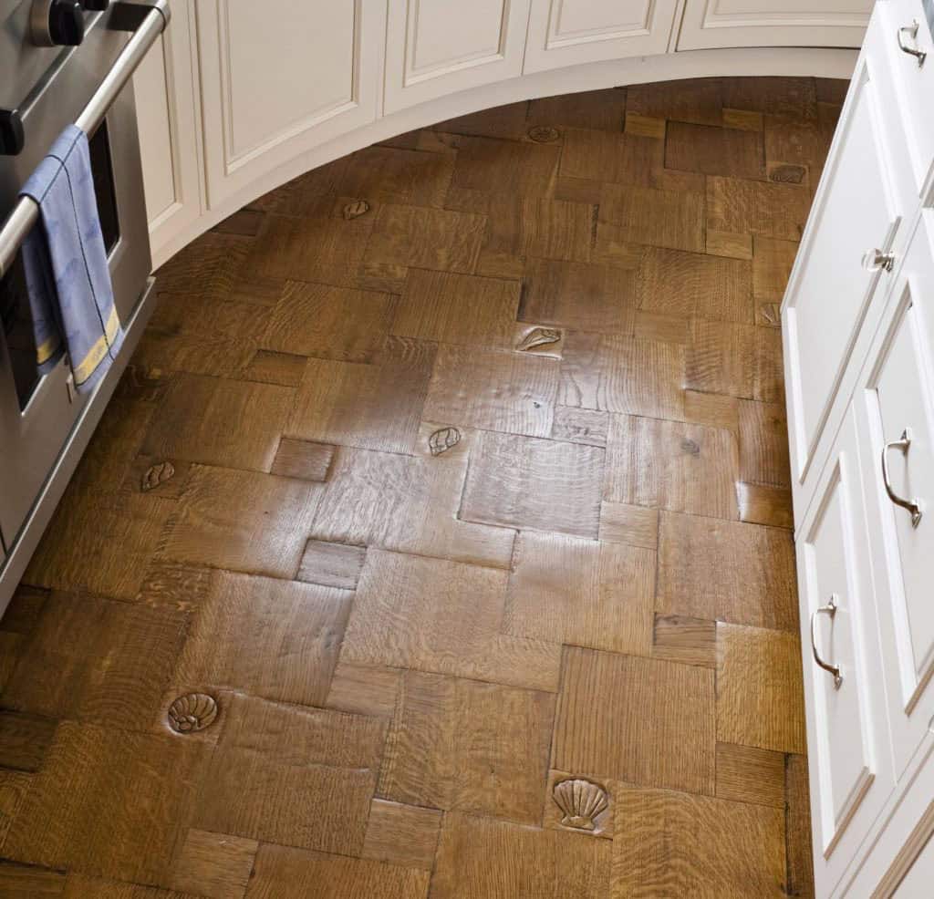 Parquet wood floor with carved seashell motifs in a basket-weave pattern beneath curved white kitchen cabinetry