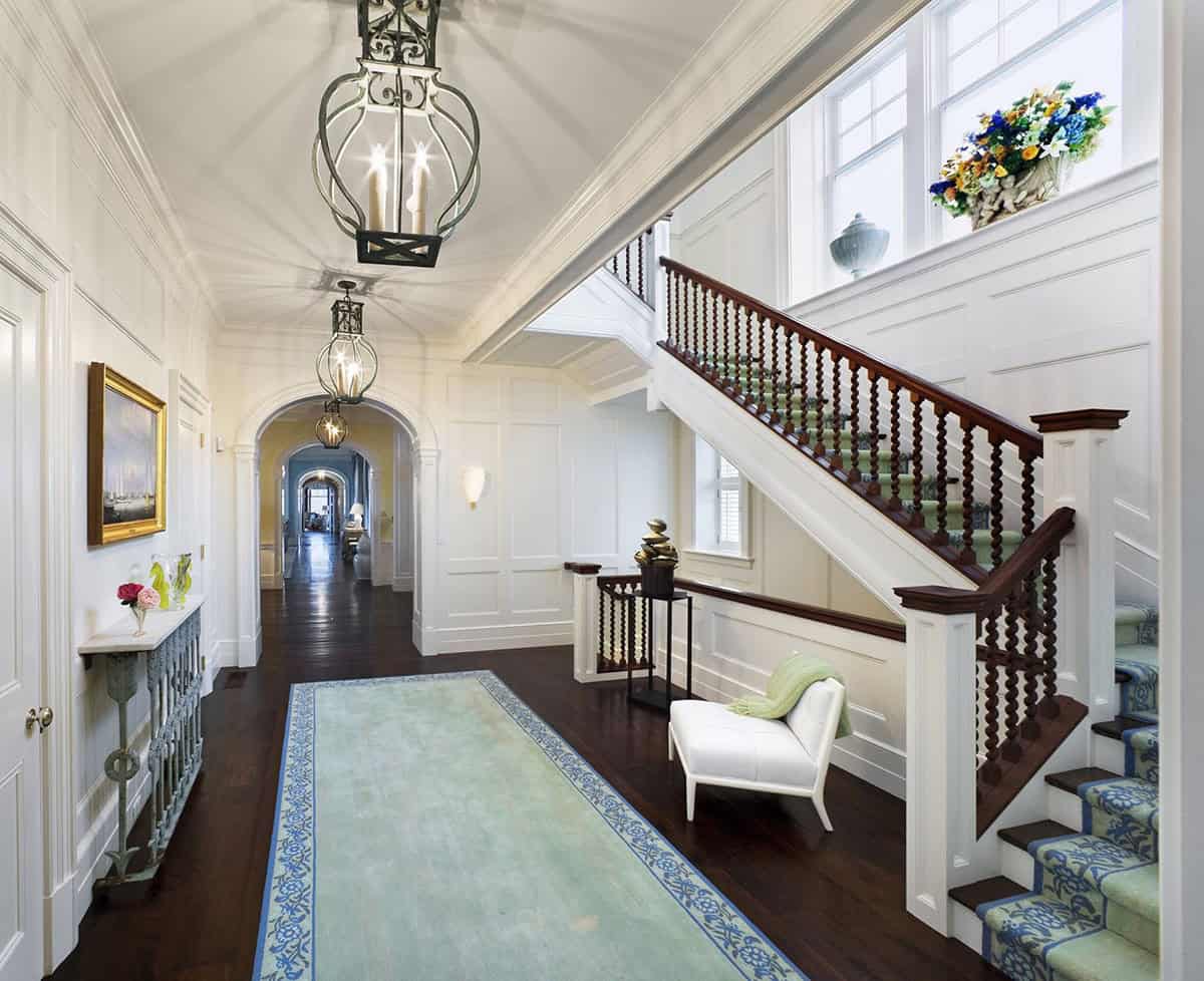 Grand hallway with barrel-vaulted ceiling, wainscoting, iron lanterns, arched doorways, and dark hardwood floors leading to a staircase