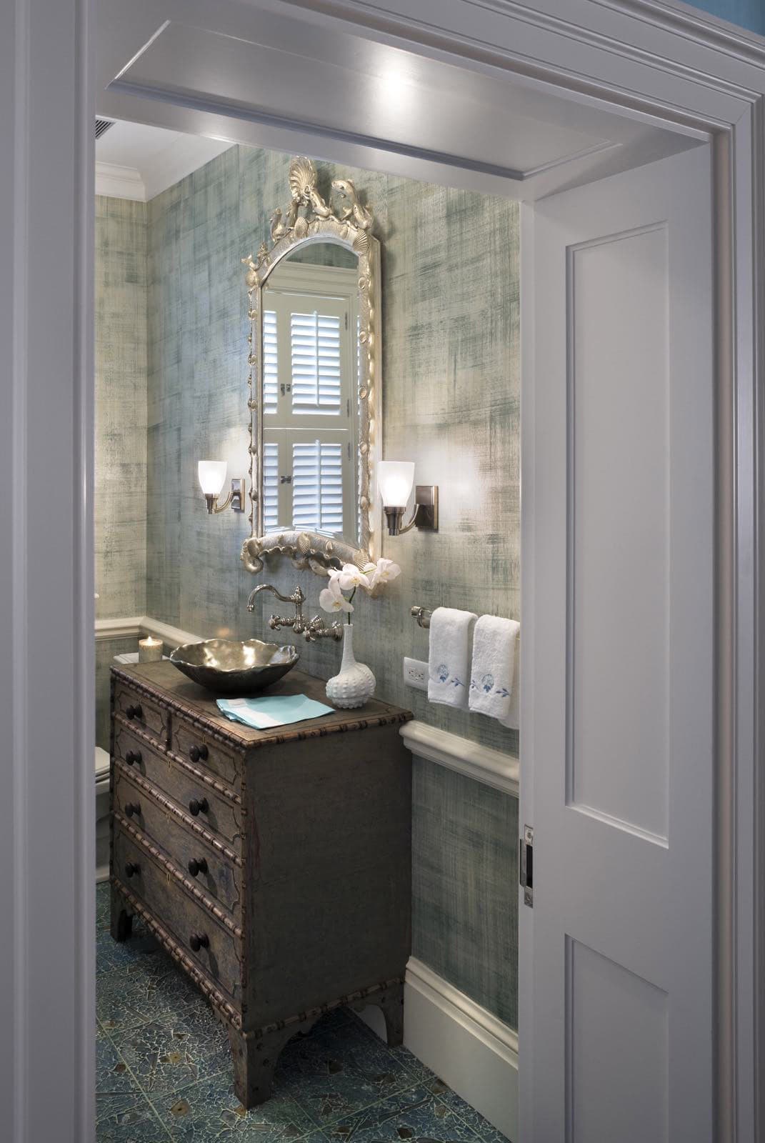 Powder room with antique bamboo-carved dresser vanity, silver vessel sink, shell-framed mirror, and textured sea-green wallcovering