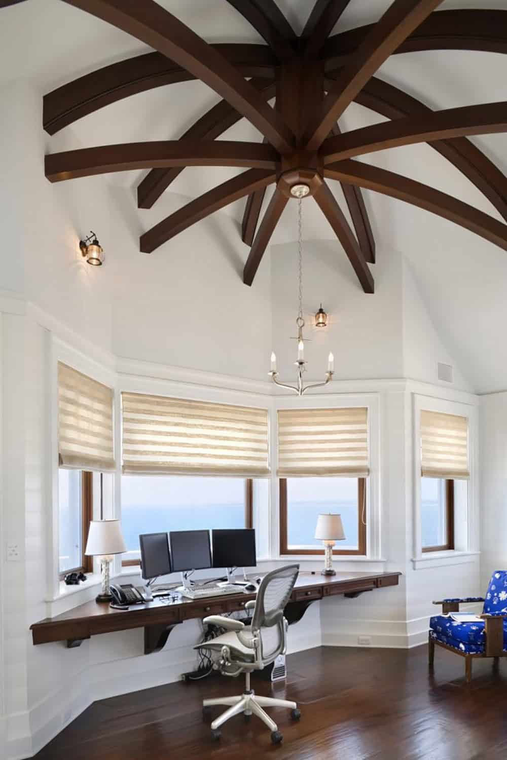 Home office with dramatic starburst ceiling beams, wrap-around floating desk, anchor chandelier, and panoramic ocean views through bay windows