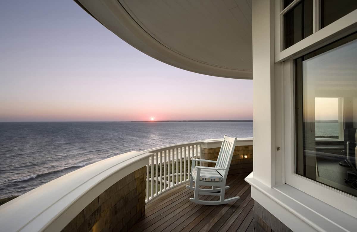 Curved upper balcony with white rocking chair overlooking a tranquil ocean sunset