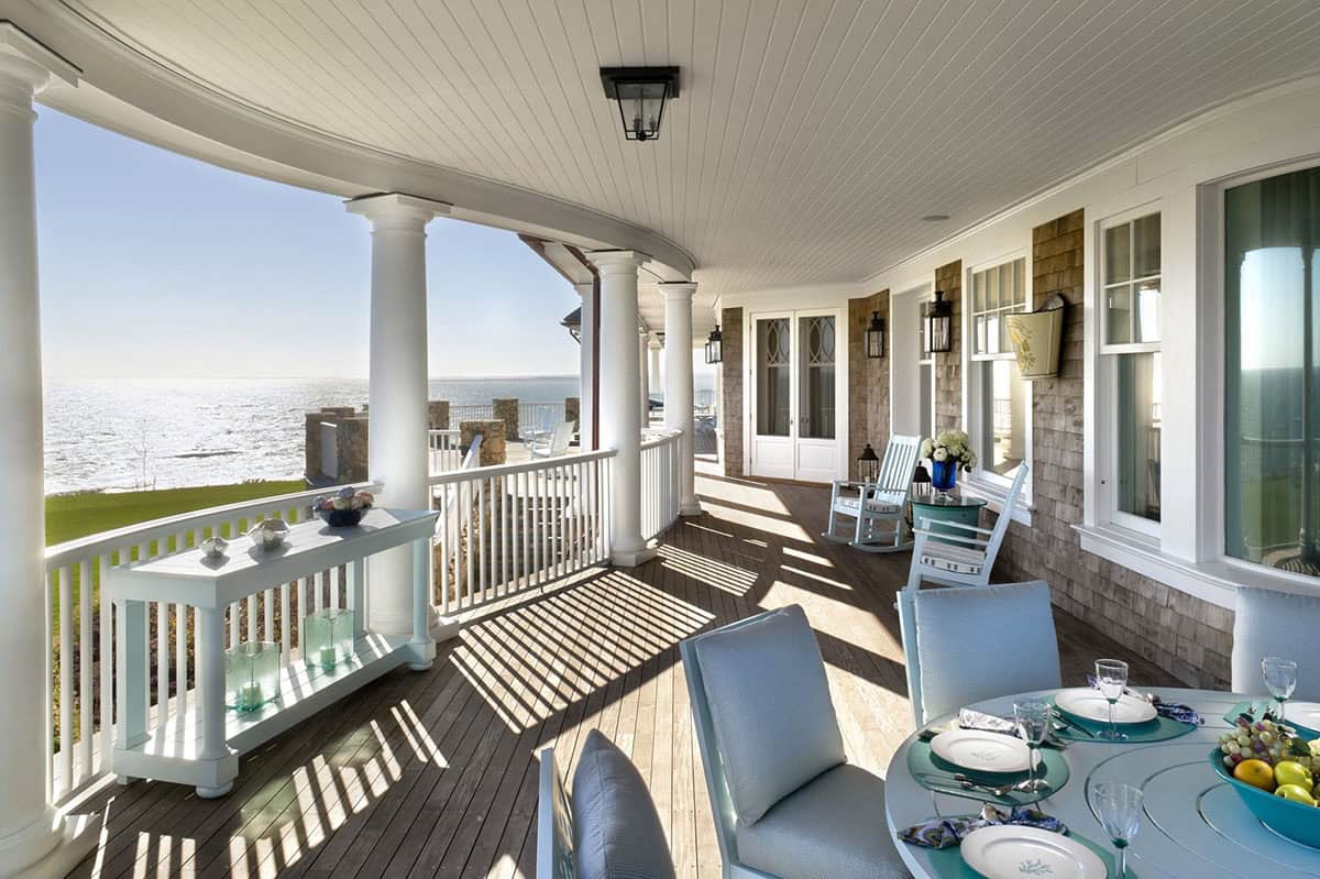 Wraparound covered porch with white columns, outdoor dining set, and sweeping ocean views
