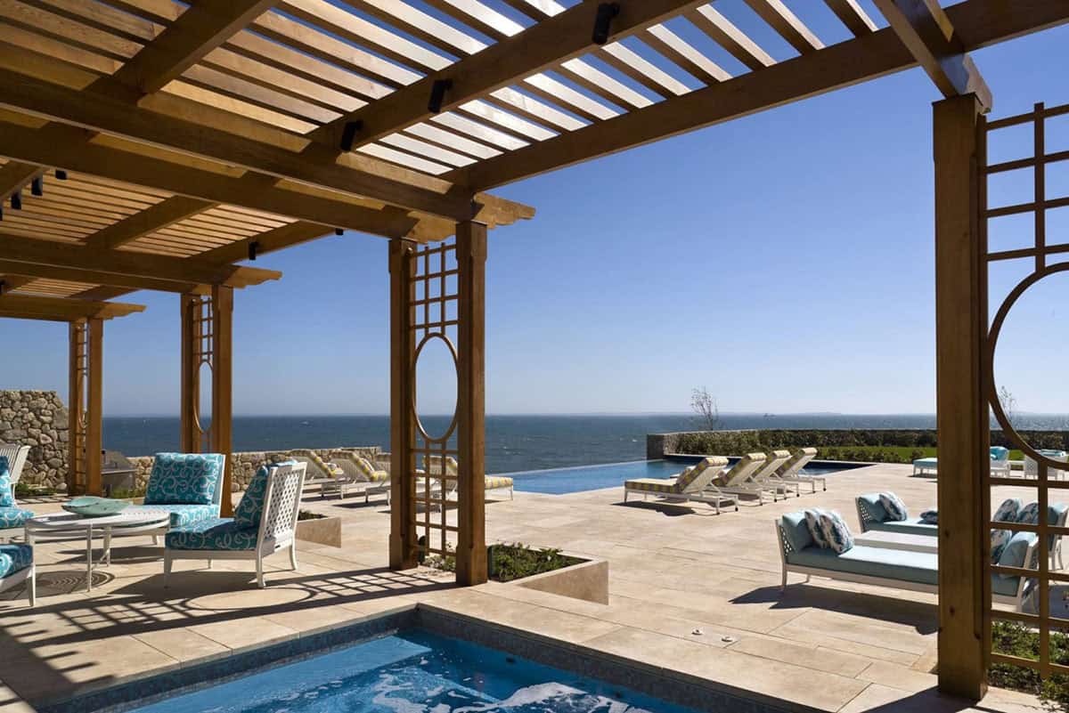 Wood pergola with decorative lattice panels framing an oceanfront pool terrace with turquoise outdoor seating