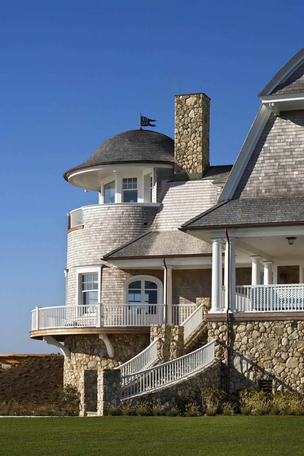 Shingle-style turret with conical roof, curved balconies, stone base, and a flag dated 2007