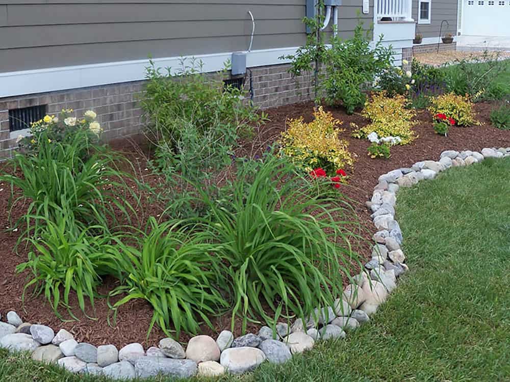 Close-up of smooth river rock edging bordering a mulched front garden bed with daylilies and colorful shrubs