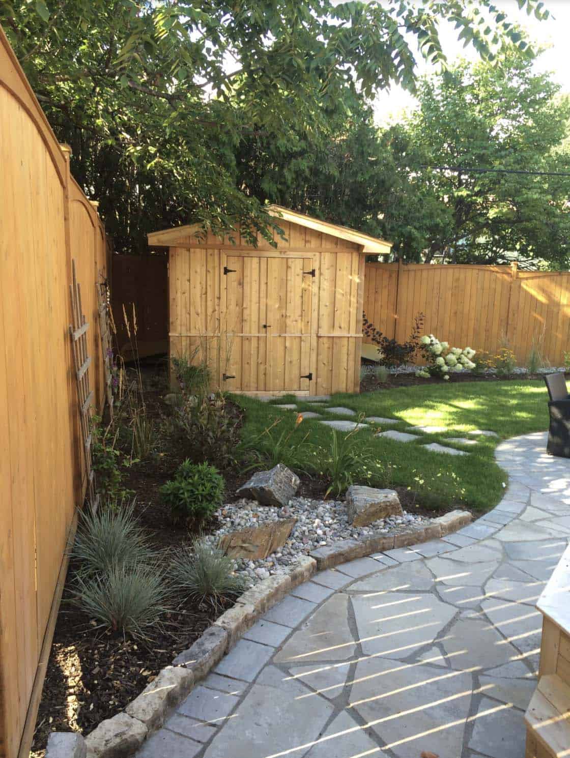 Curved ledgerock stone edging with natural texture bordering a mulched garden bed beside a flagstone patio