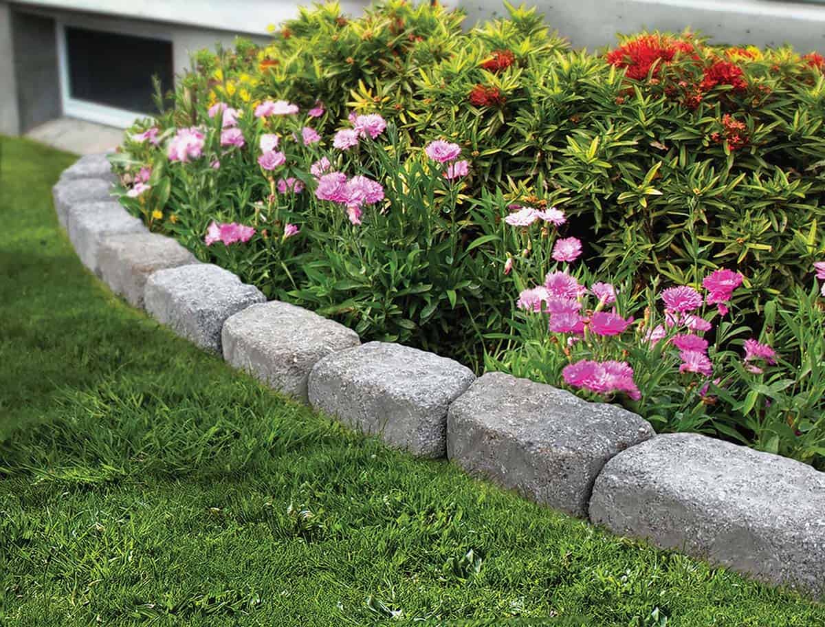 Grey granite block edging along a curved garden bed with pink dianthus and flowering shrubs beside a lawn