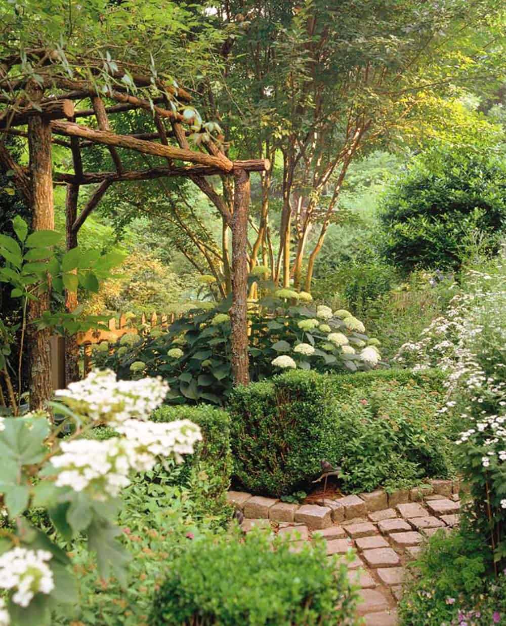 Brick cobblestone path edged with Korean boxwood hedging and white hydrangeas beneath a rustic log pergola