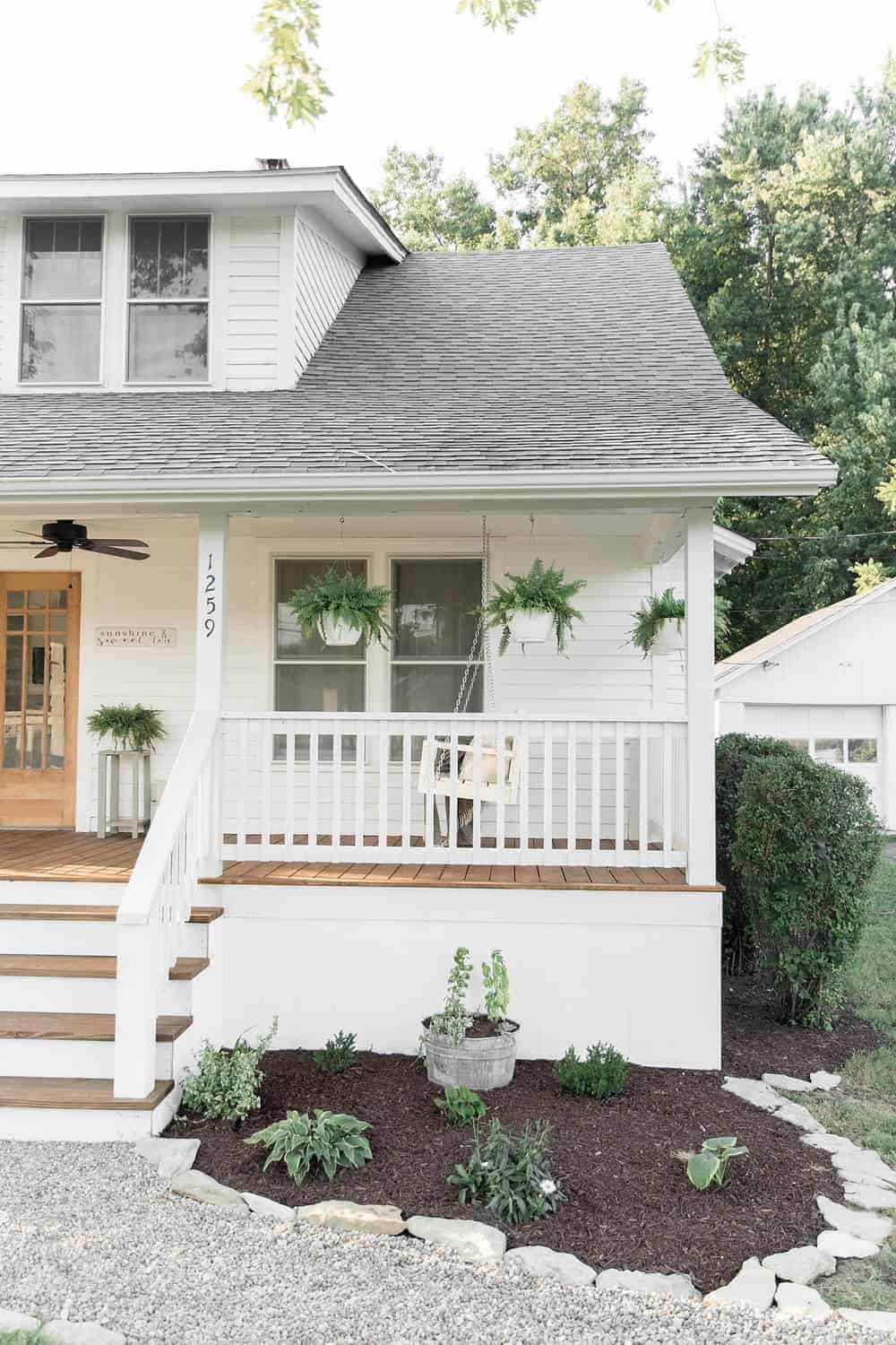 White creek stone edging along a mulched front garden bed with hostas beneath a classic white farmhouse porch