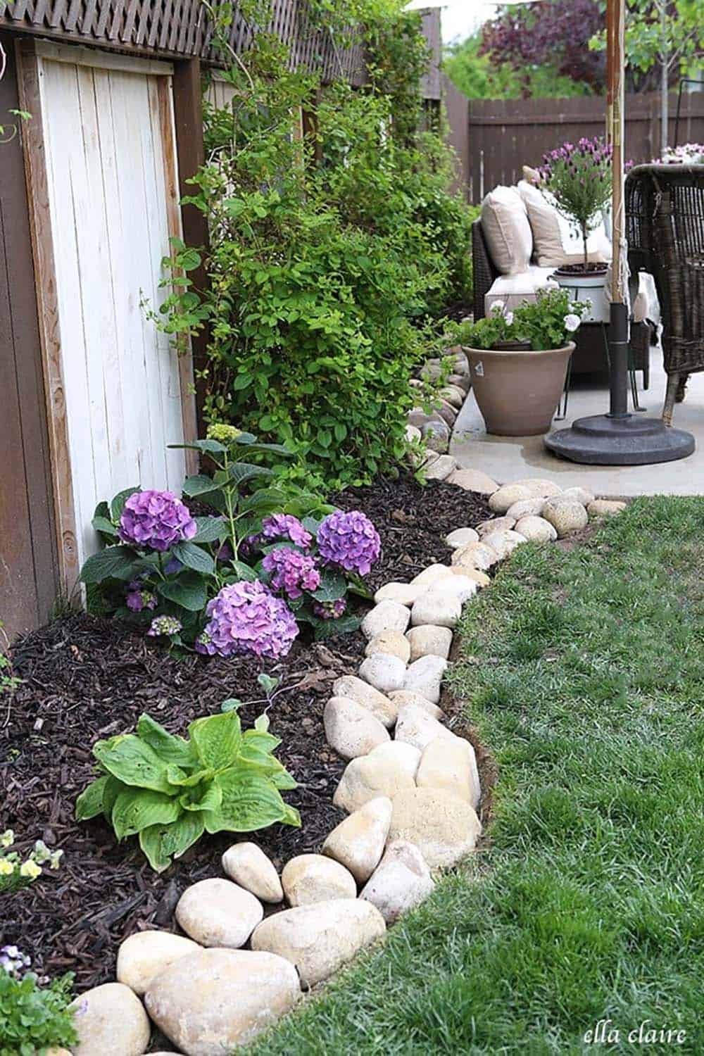Pale limestone rock edging along a narrow side garden bed with purple hydrangeas and hostas beside a patio