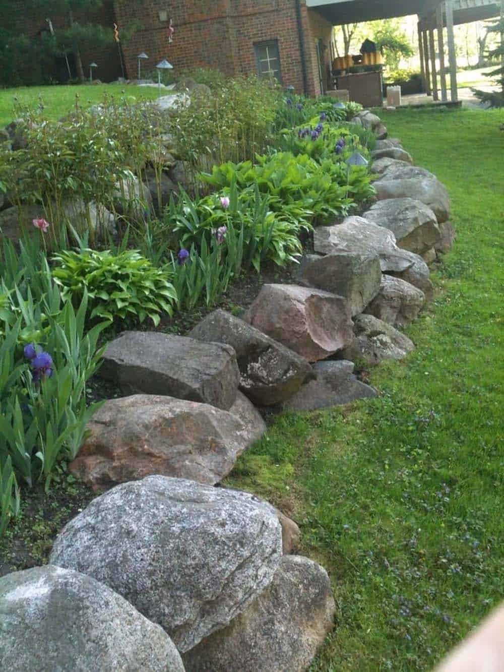 arge granite boulders forming a sweeping retaining border along a garden bed with irises and hostas beside a brick home