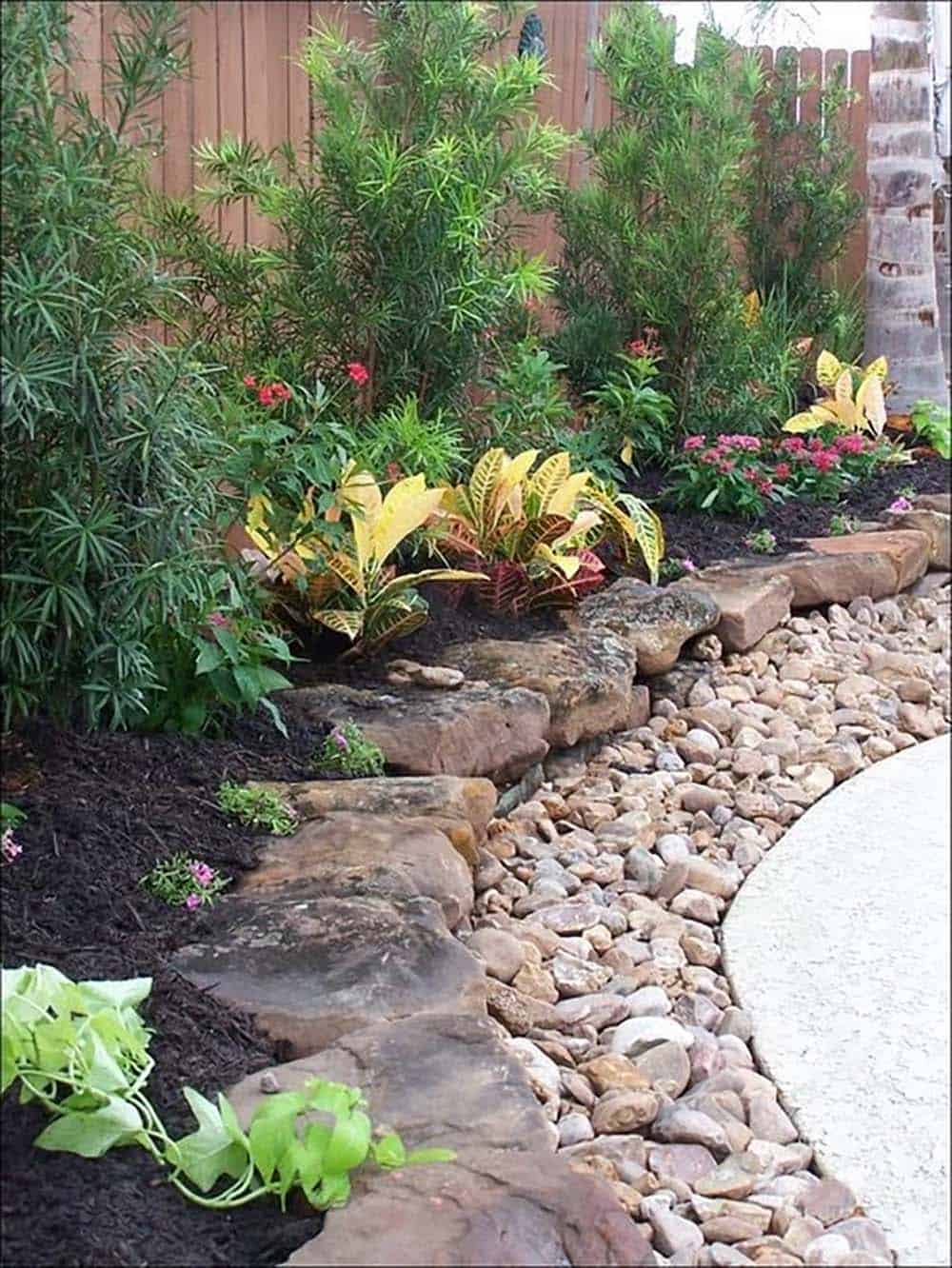 Layered natural limestone rock edging with a river rock channel bordering a tropical garden bed with crotons and ixora