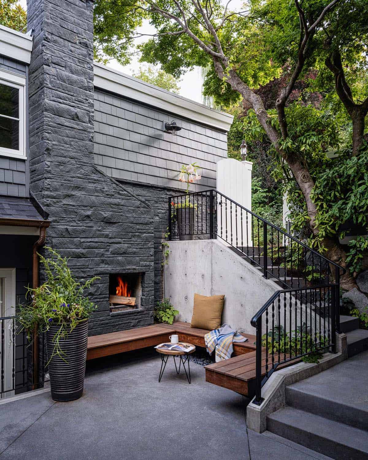 Outdoor patio with dark stone fireplace, built-in wood bench seating, and concrete retaining wall