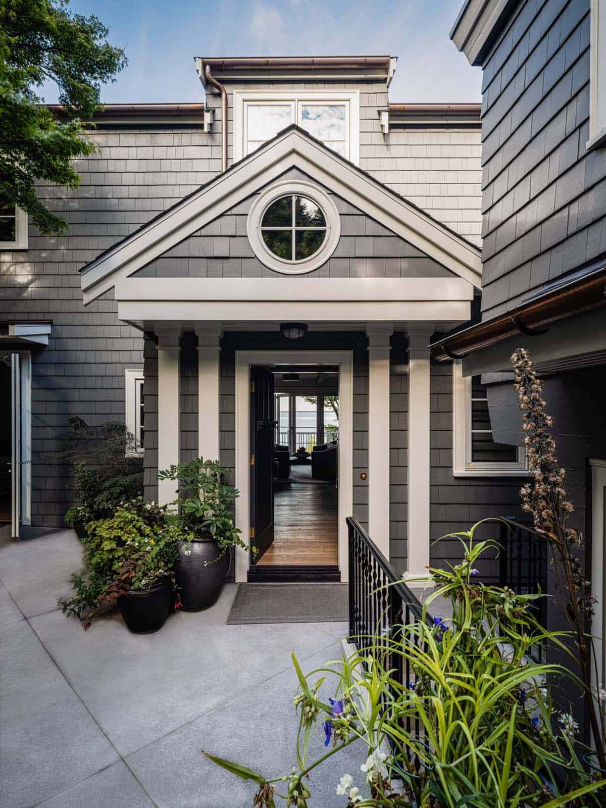 Covered front entry portico with round window, white columns, and view through hallway to Puget Sound