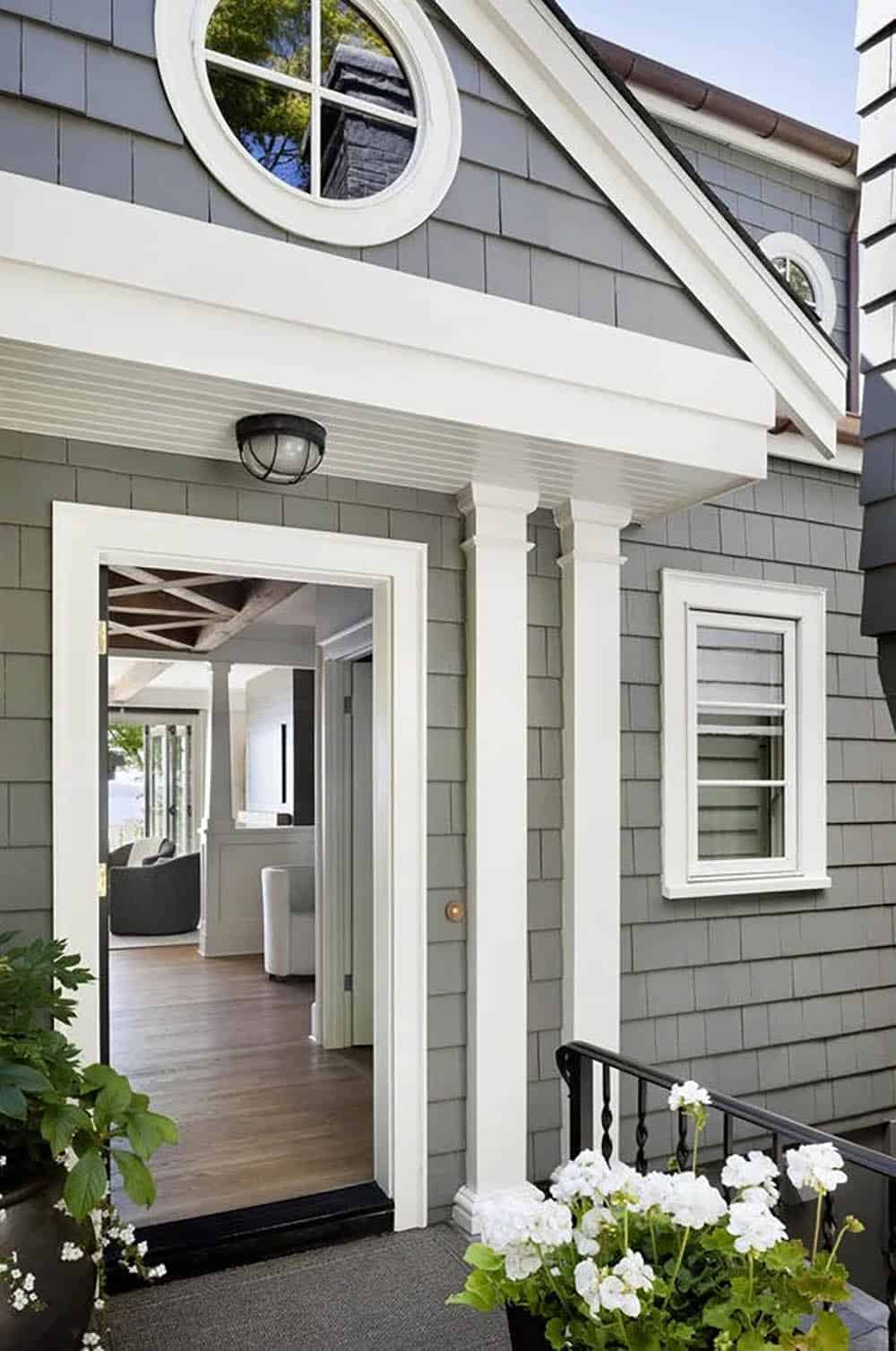 Close-up of home's covered entry with circular porthole window, white columns, and beadboard ceiling