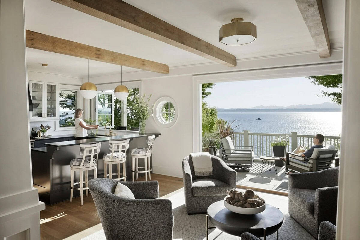 Open-plan living area with exposed wood beams, kitchen beyond, and panoramic Puget Sound view through folding doors