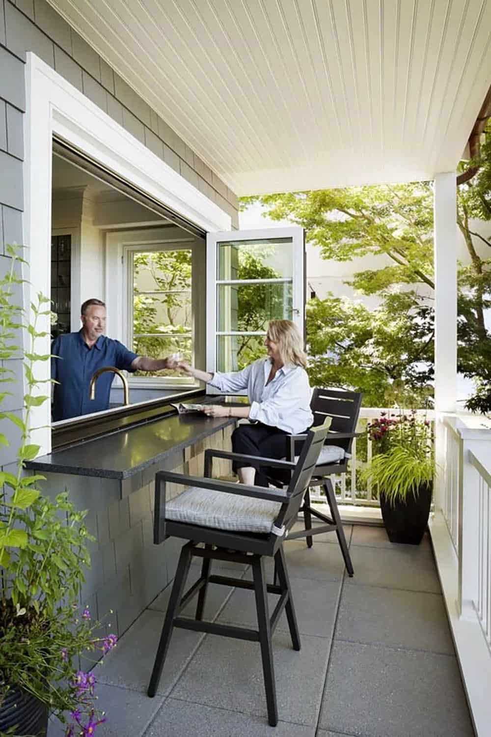Pass-through kitchen window serving as outdoor bar counter on covered porch with bar seating