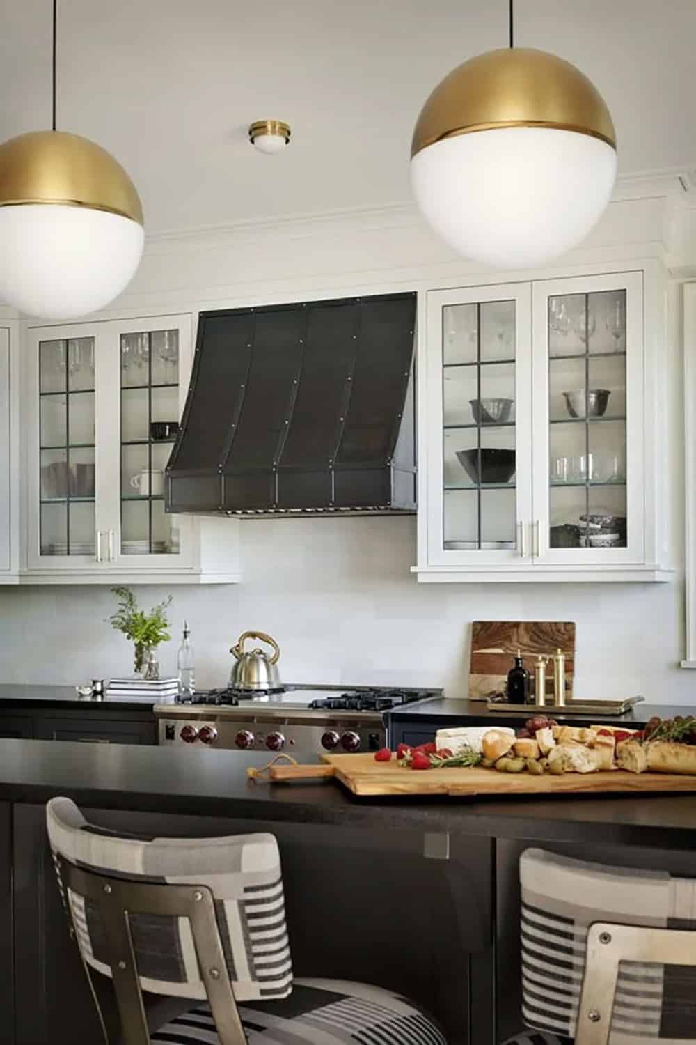 Kitchen with white upper cabinets, dark island, black range hood, and large gold globe pendant lights