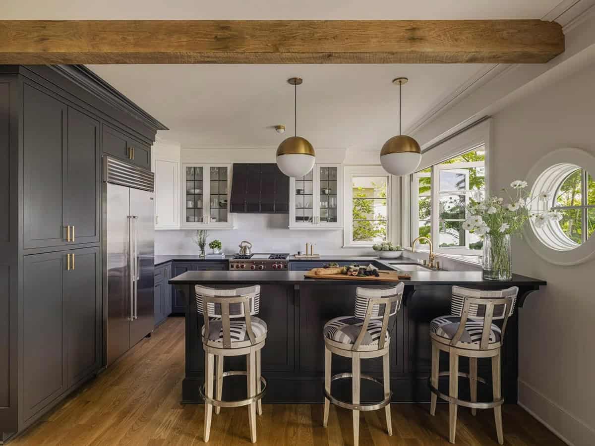 Full kitchen view with dark lower cabinets, white uppers, wood beam, gold pendants, and porthole window