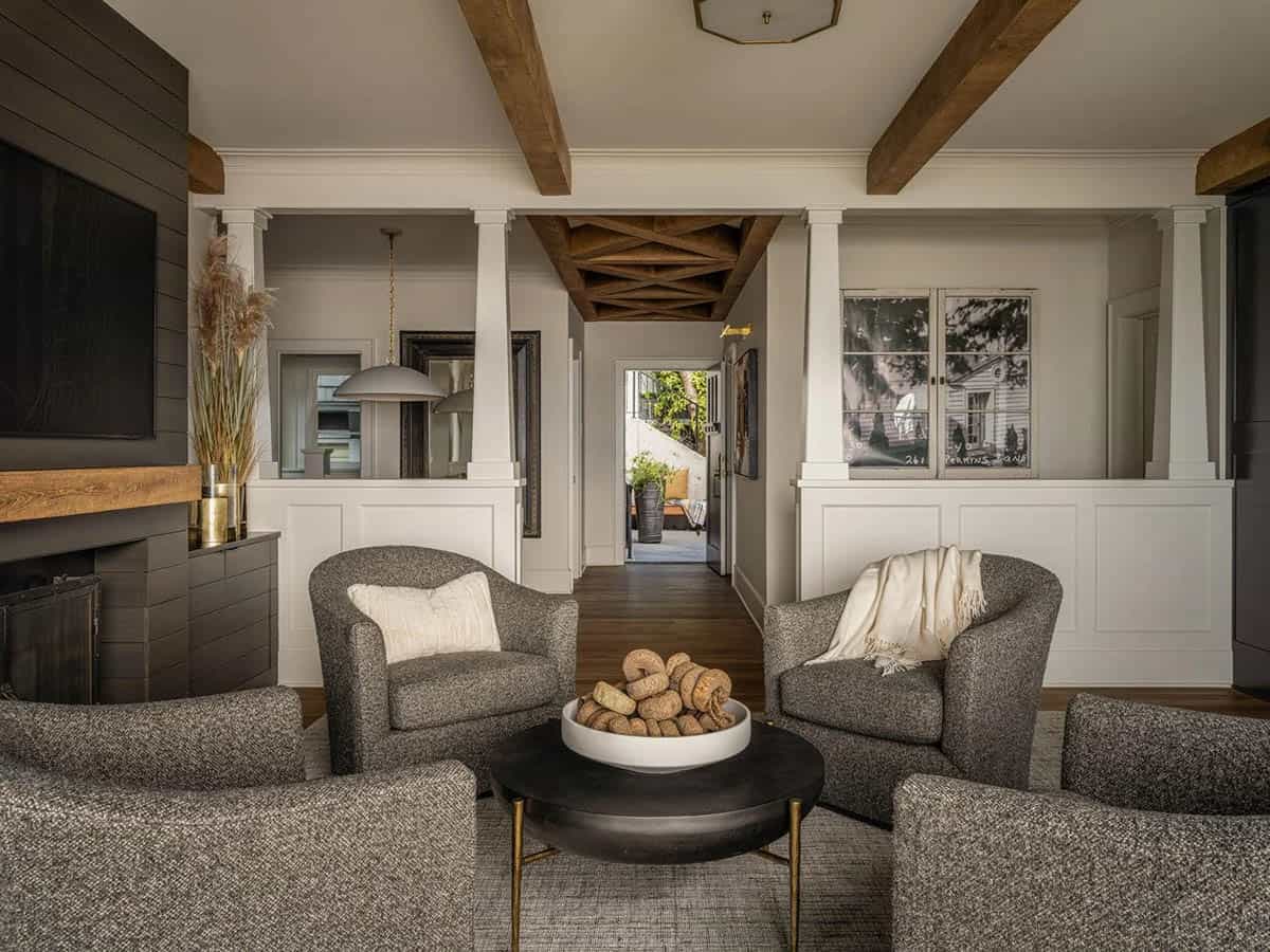 Living room with gray swivel chairs, wood beam ceiling, fireplace, and view to entry hallway