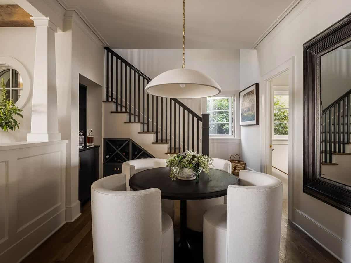 Intimate dining area with round dark table, white curved chairs, dome pendant, and under-stair wine storage