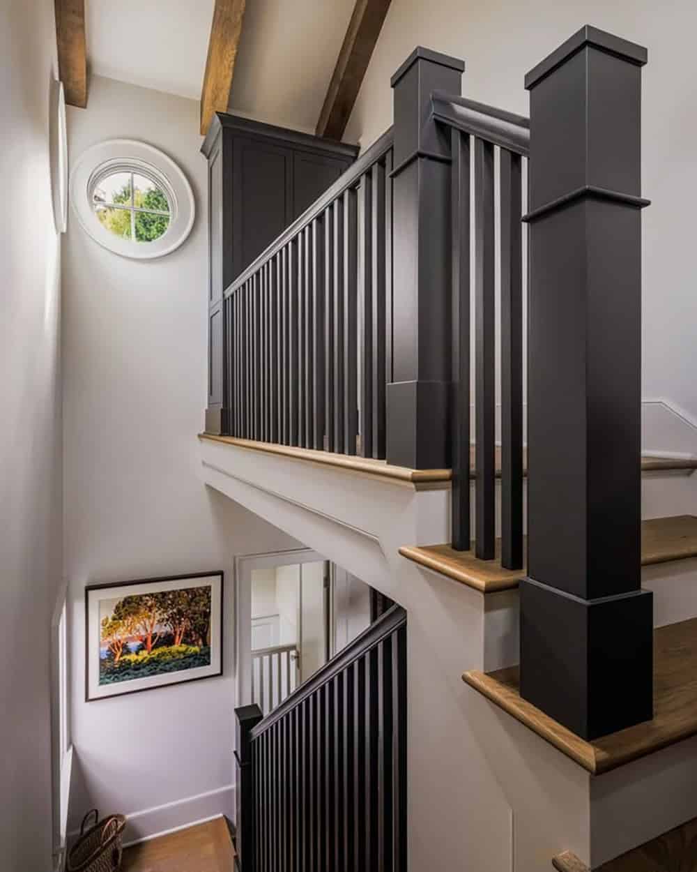 Staircase with dark painted balusters, wood handrail, and porthole window with exposed timber ceiling