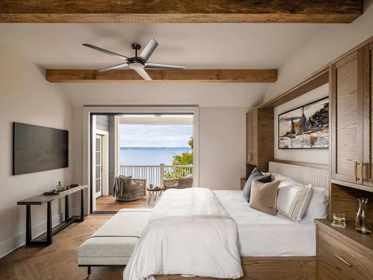 Primary bedroom with wood beams, herringbone floor, built-in oak cabinetry, and waterfront balcony view