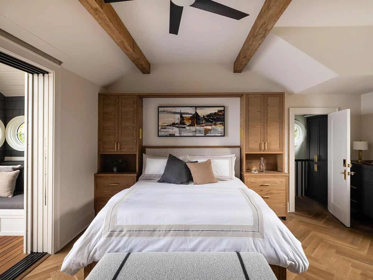 Primary bedroom with vaulted ceiling, exposed beams, flanking built-in oak wardrobes, and herringbone floor