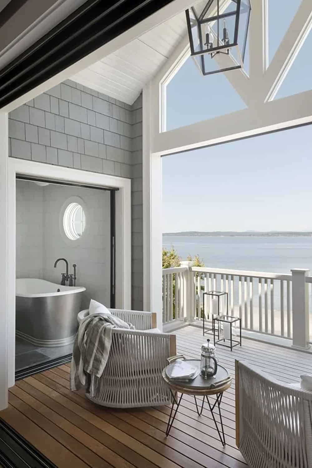 Covered waterfront deck with rope lounge chair, soaking tub visible through open door, and panoramic Puget Sound view
