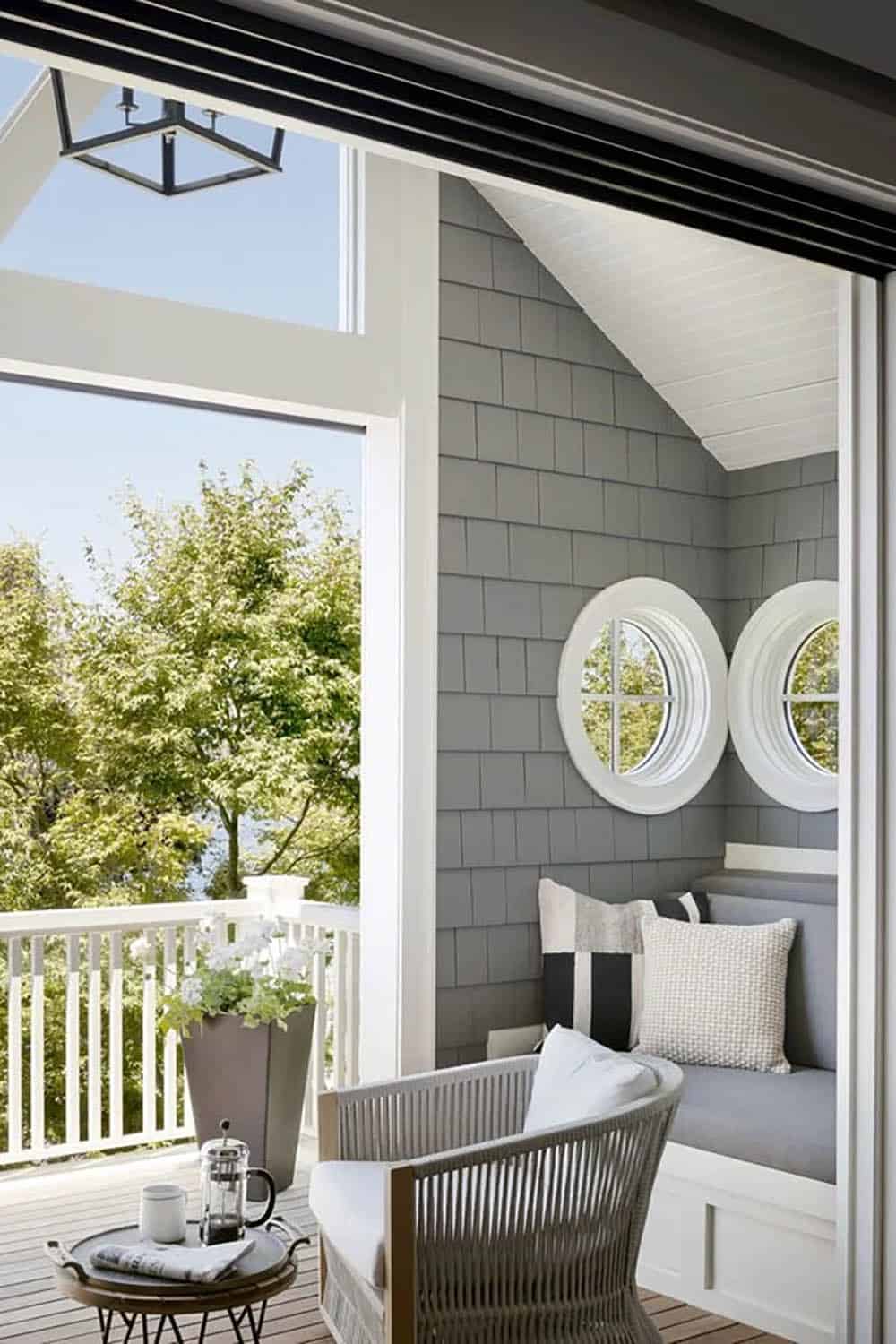 Screened sleeping porch nook with built-in bench, twin porthole windows, and rope lounge chair on wood deck