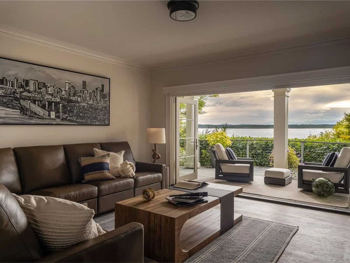 Lower-level living room with leather sofa, wood coffee table, Seattle skyline artwork, and waterfront terrace view at dusk