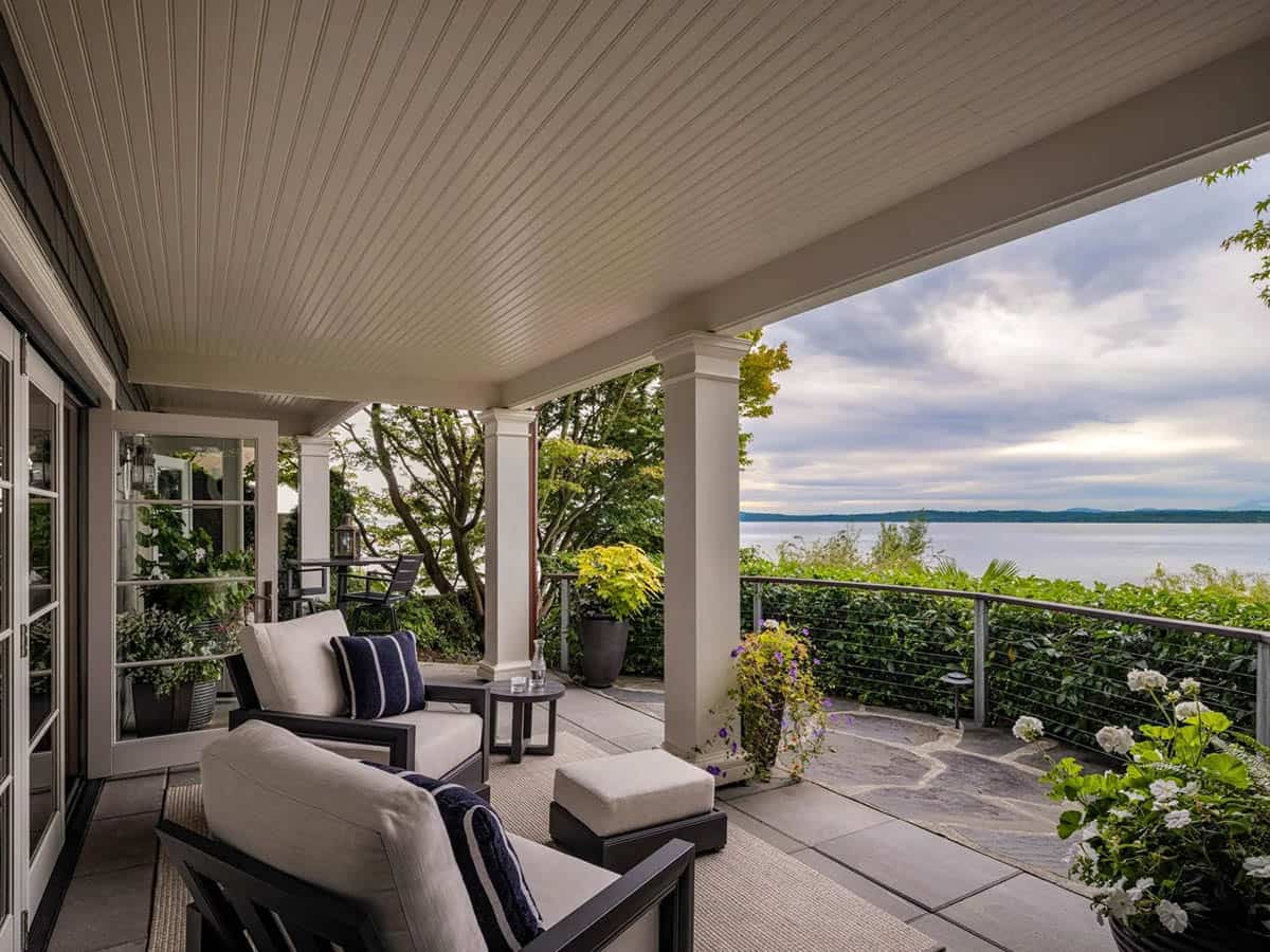 Covered waterfront porch with white columns, beadboard ceiling, cushioned lounge chairs, and expansive Puget Sound view