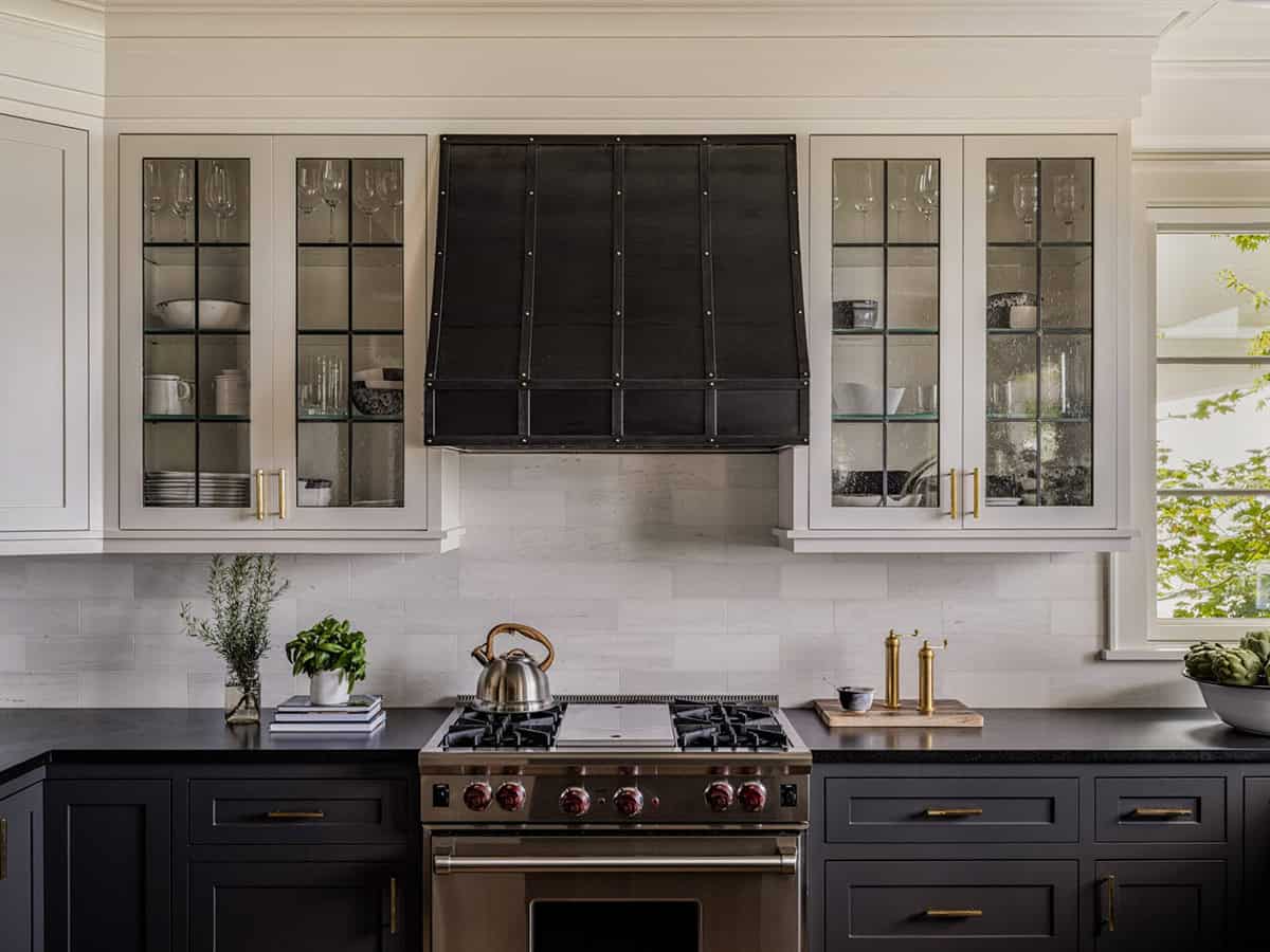 Kitchen cooking wall with dark cabinetry, custom black riveted range hood, glass upper cabinets, and Wolf range