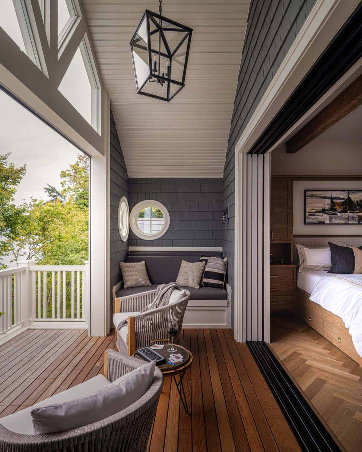 Covered sleeping porch with built-in bench nook, porthole window, rope lounge chairs, and view into primary bedroom