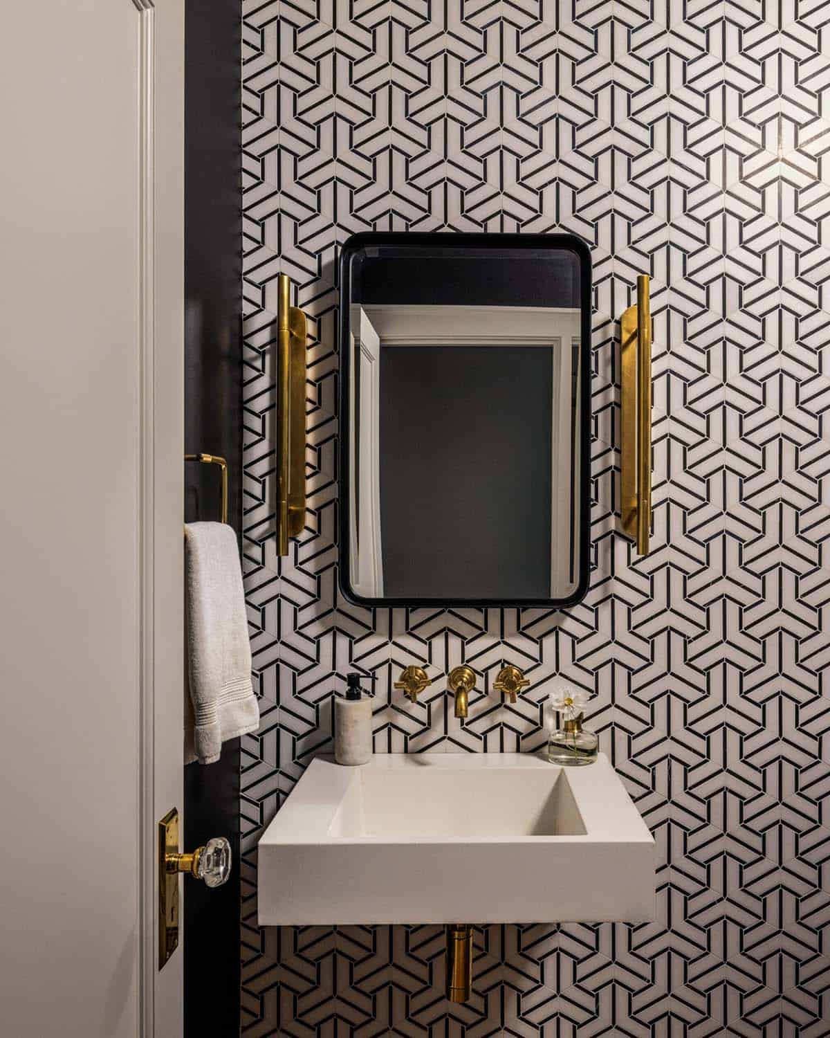 Powder room with floor-to-ceiling geometric black-and-white tile, floating white sink, black mirror, and brass fixtures