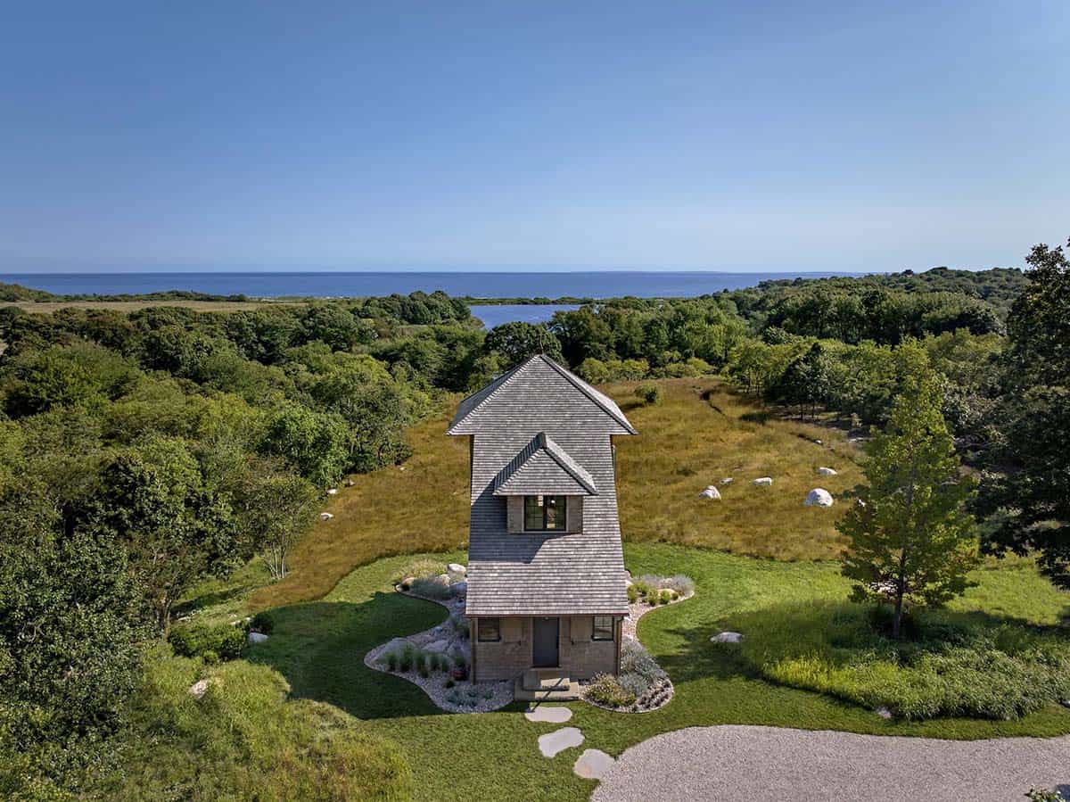 Aerial view of shingle-style tower house rising above meadow with ocean glimpse beyond
