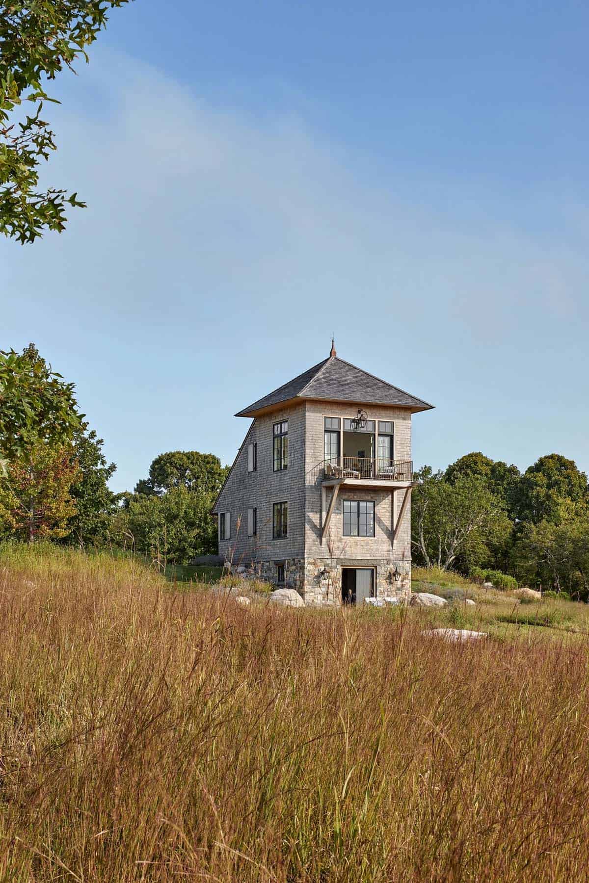 Tall shingle tower house rising from golden meadow grasses with upper balcony