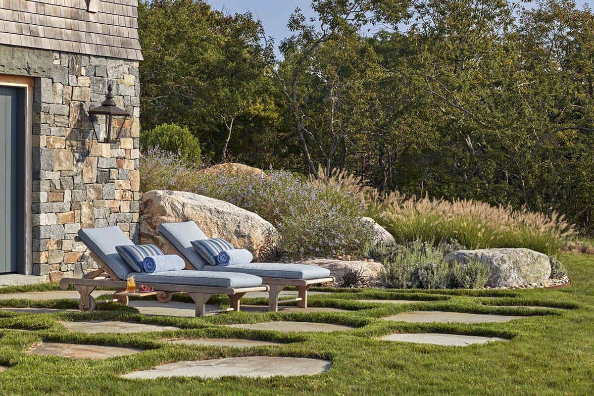 Teak lounge chairs beside stone base of tower house with native boulder garden landscaping