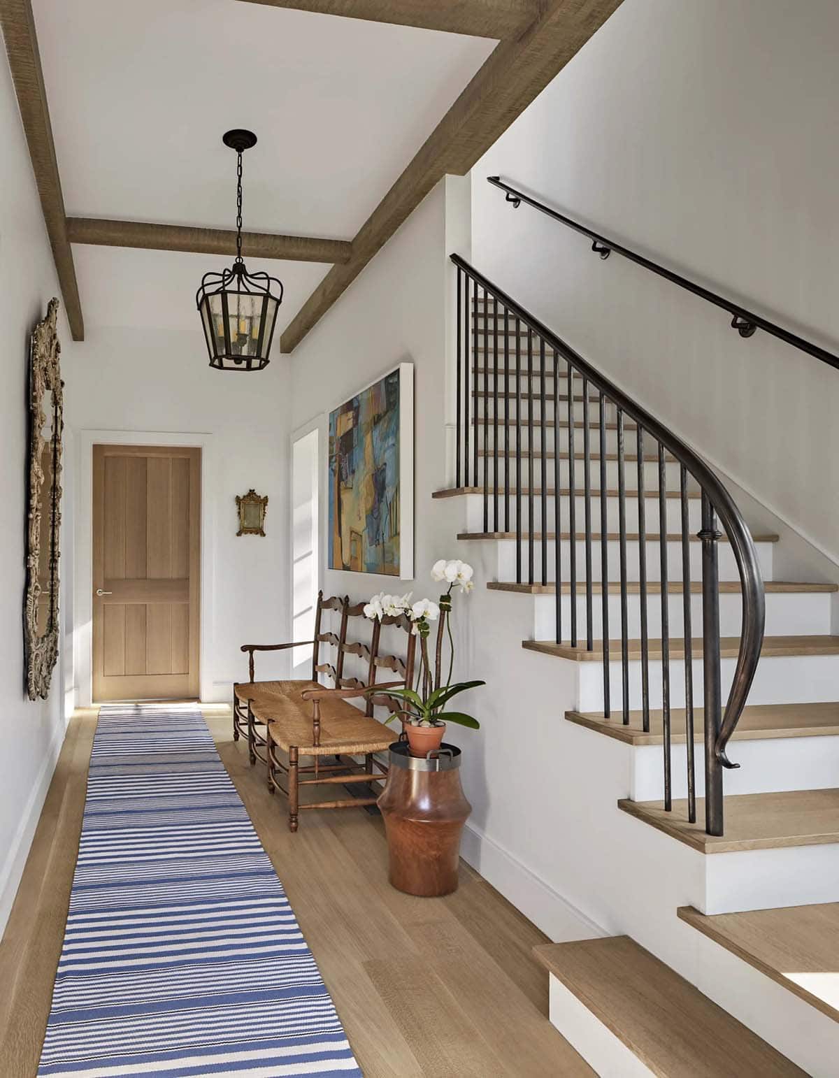 Foyer with wood beam ceiling, iron staircase, striped runner rug, and antique bench
