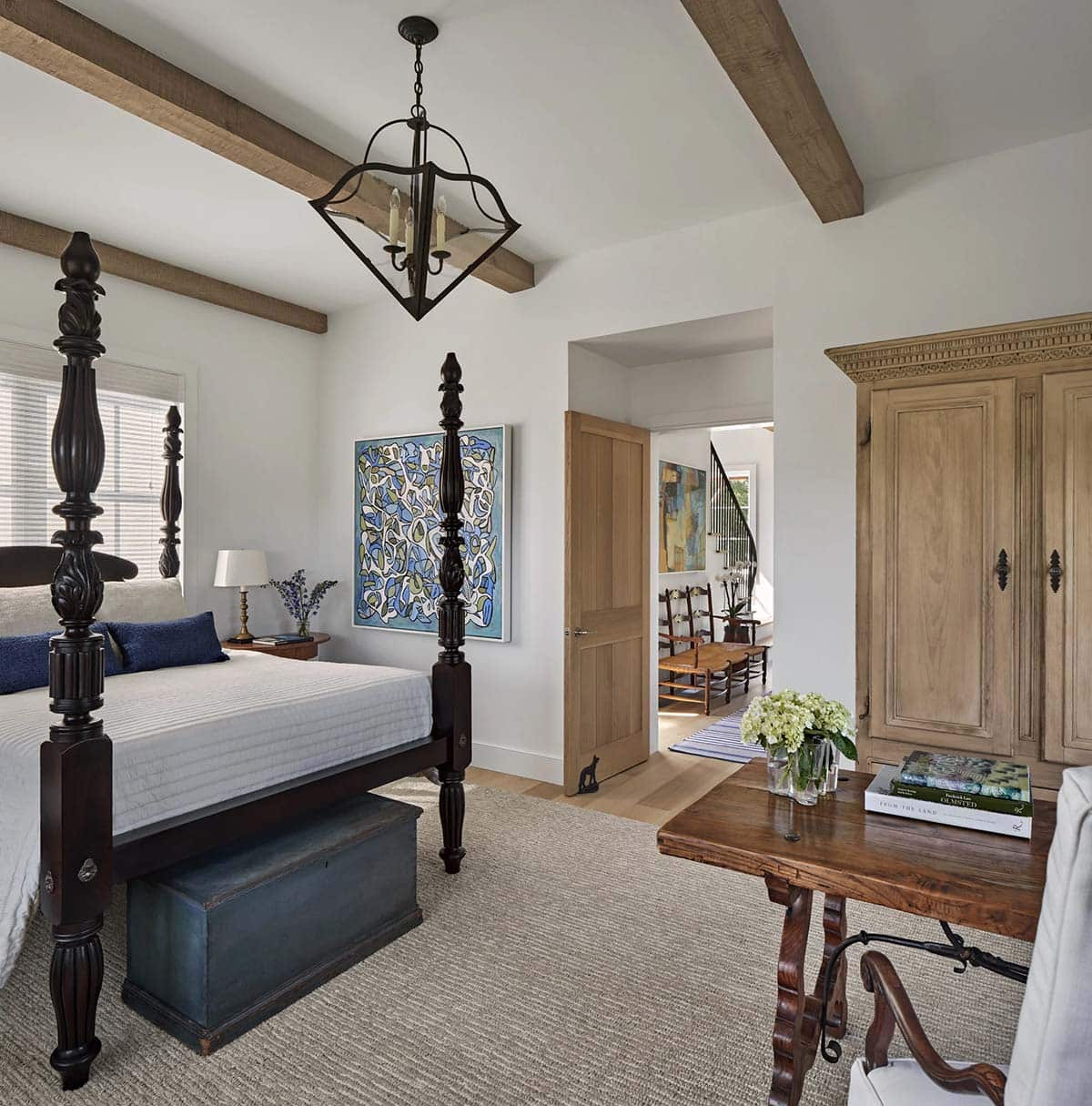 Primary bedroom with ornate dark four-poster bed, exposed beams, antique armoire, and colorful artwork