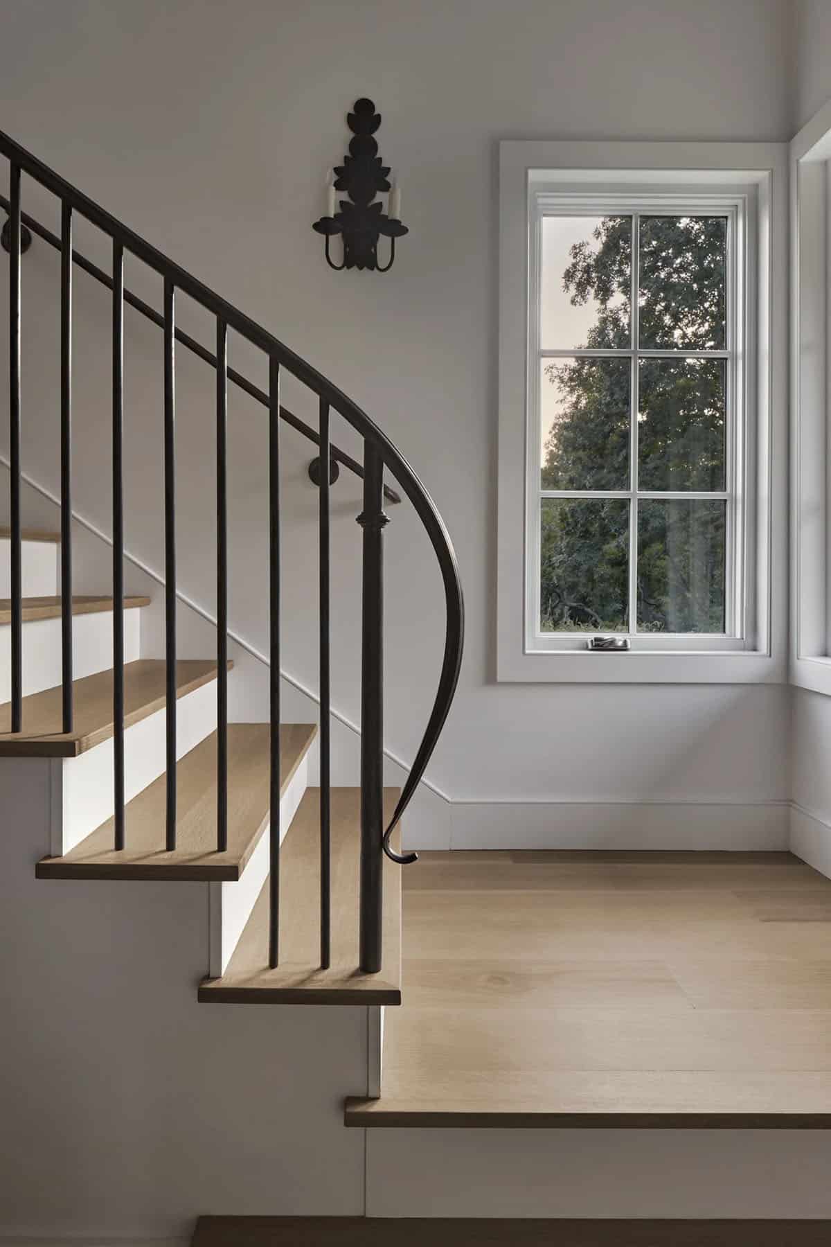 Close-up of curved iron staircase railing with oak treads and ornate wall sconce