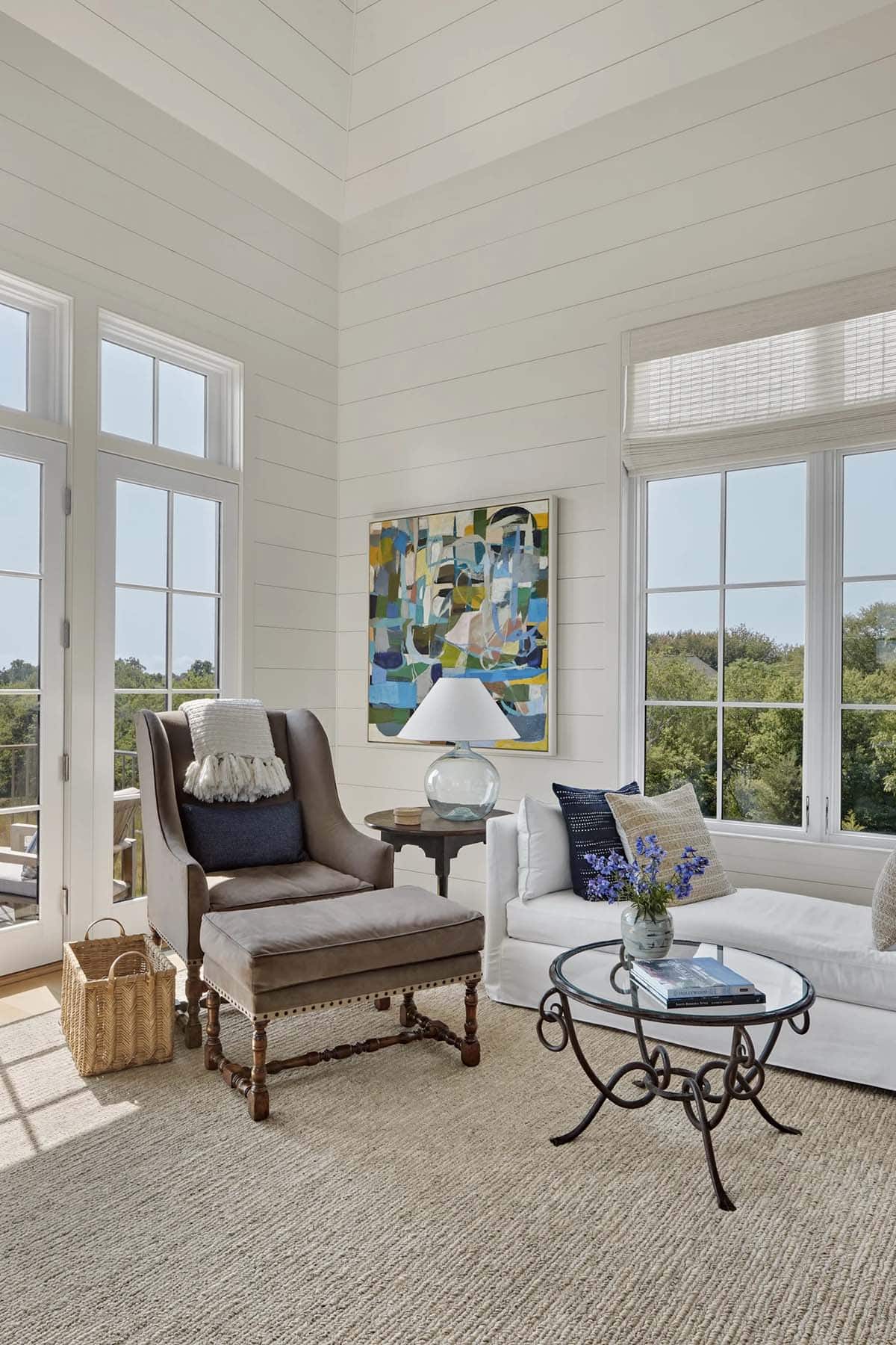 Sun-filled sitting room with shiplap walls, wingback chair, white sofa, and abstract artwork