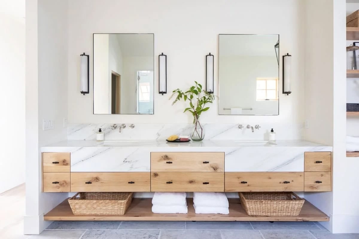 Primary bathroom double vanity with floating oak cabinet, white marble countertop, and black-framed mirrors
