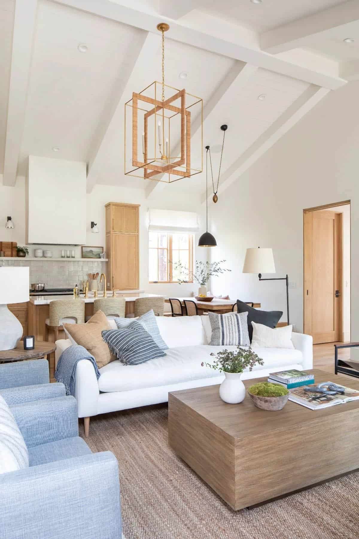 Bright open-plan living room with white vaulted ceilings, gold pendant lantern, and white sofa