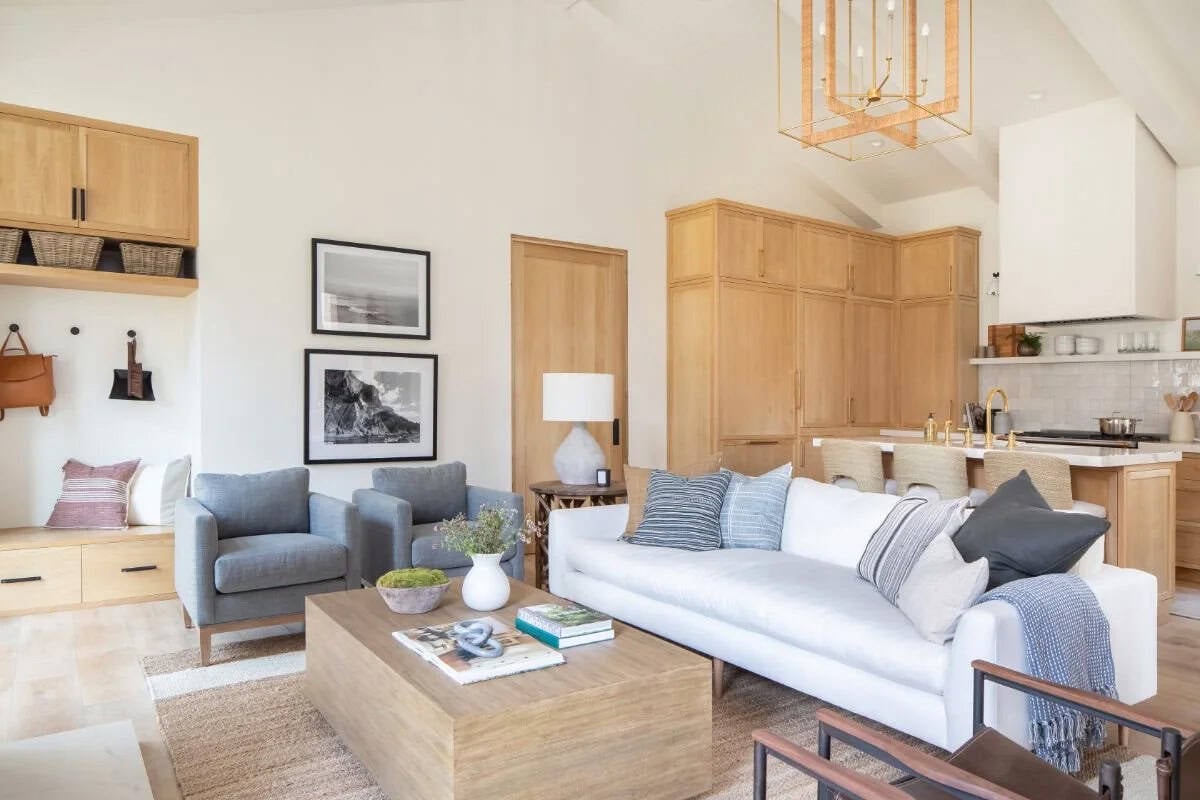 Coastal living room with white sofa, blue armchairs, wood coffee table, gold lantern pendant, and built-in mudroom nook