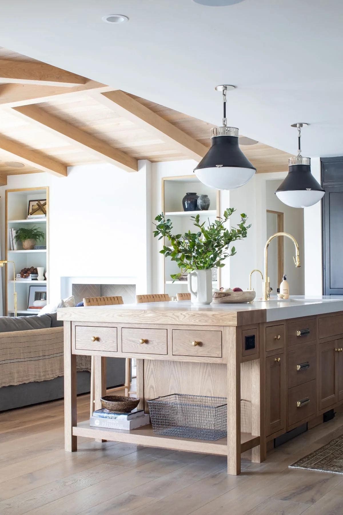 Freestanding oak kitchen island with white countertop, brass faucet, and black dome pendants under wood beam ceiling