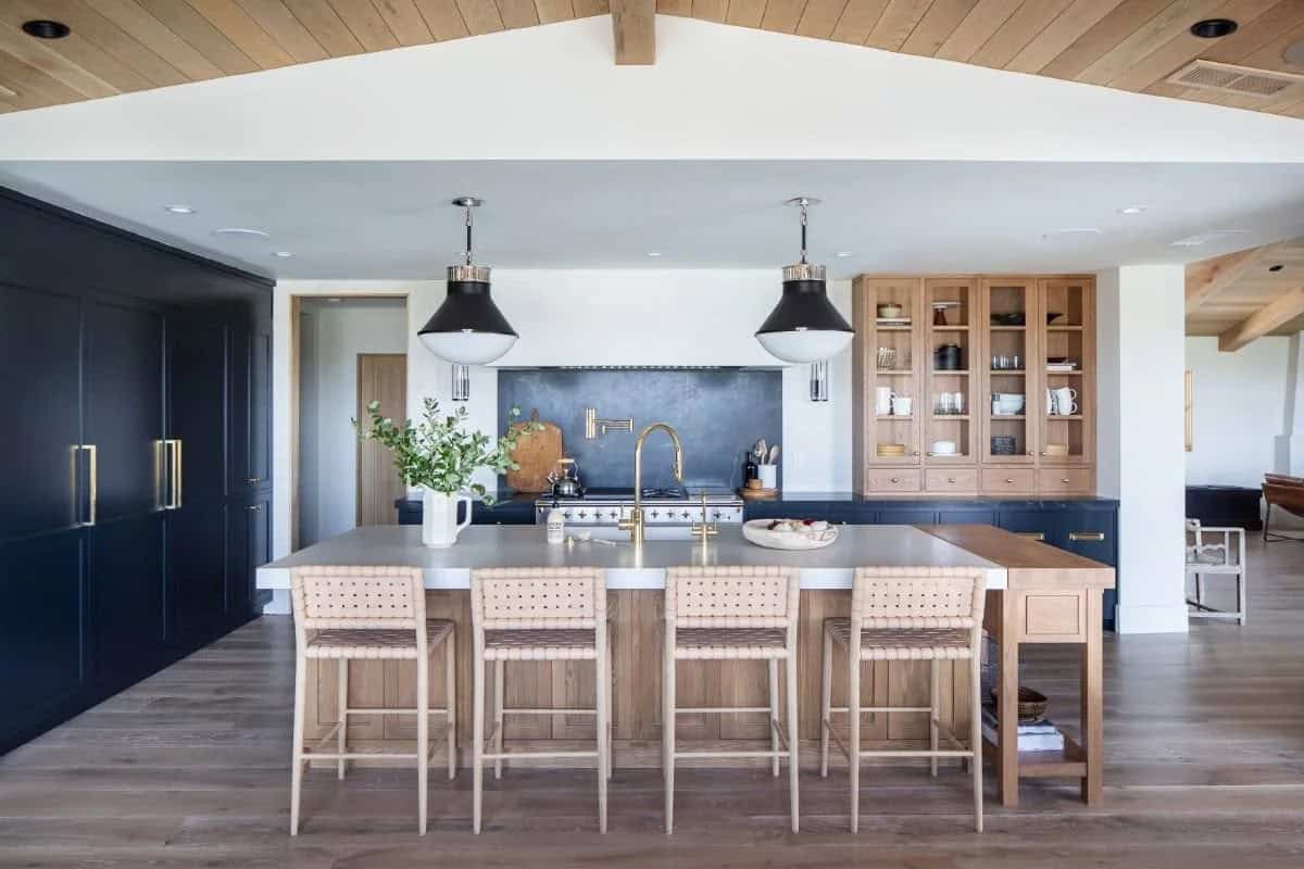 Kitchen with oak island, woven leather bar stools, navy cabinets, black pendant lights, and oak glass-front hutch