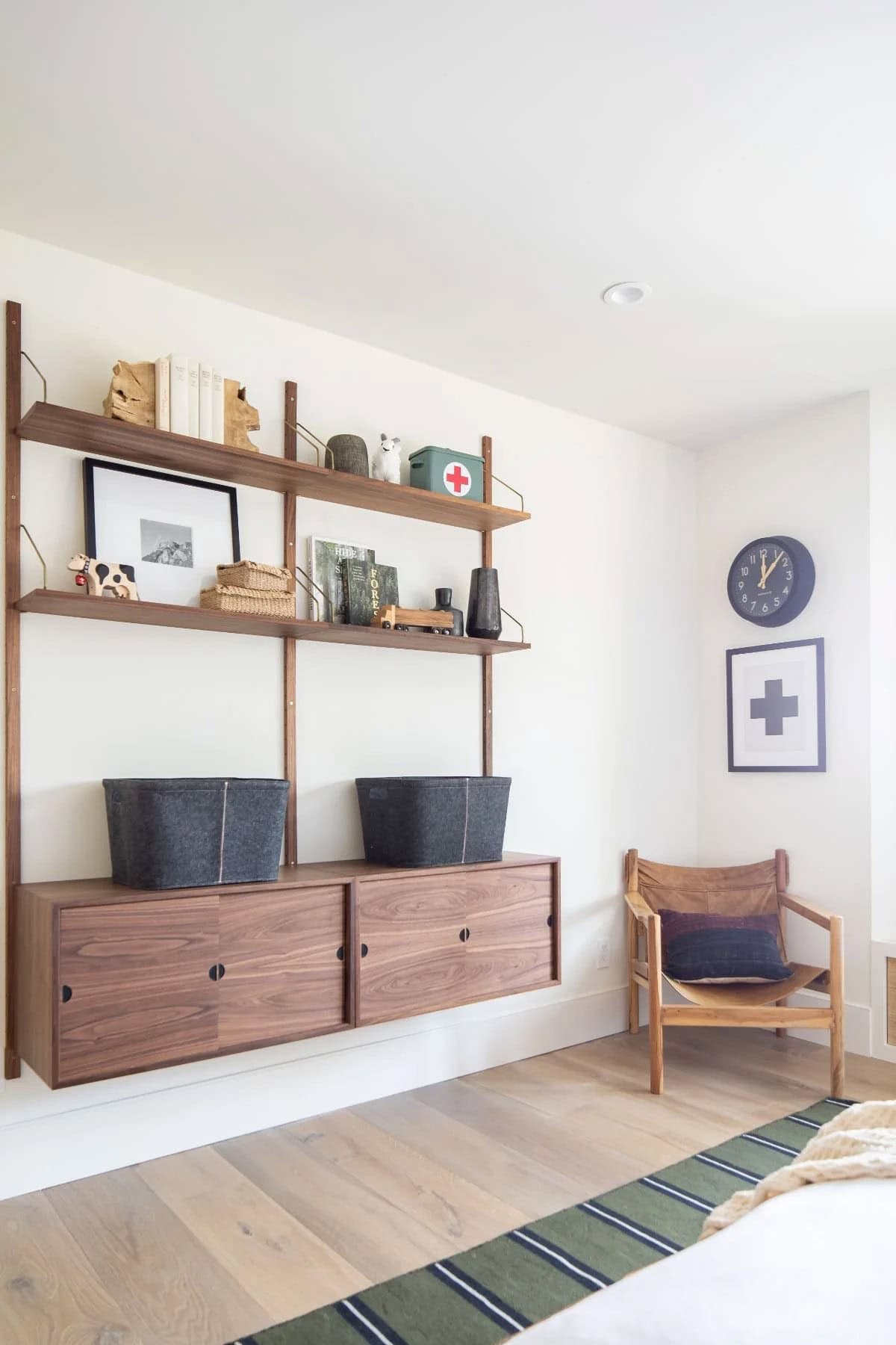Boy's bedroom with walnut wall-mounted shelving system, floating cabinet, and leather sling chair